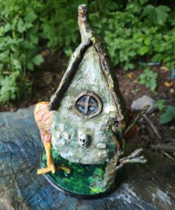 Back view of Baba Yaga Hut on chicken legs, sat on a log in a garden.