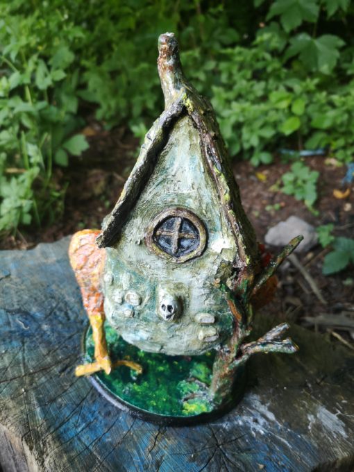 Back view of Baba Yaga Hut on chicken legs, sat on a log in a garden.