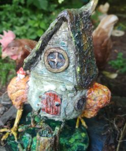 Photo of Baba Yaga Hut on chicken legs in a garden with a red hen stood behind it.