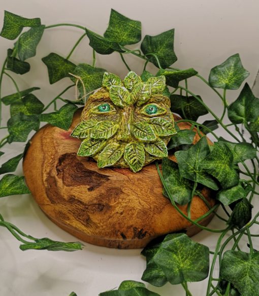small clay greenman on a wooden bowl surrounded by ivy.
