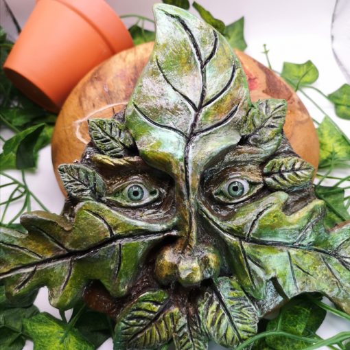 clay greenman on wooden block, with ivy and overturned plant pot in background.