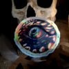 photo of a round holographic sticker of a blue and gold dragon eye. Sticker is propped against a fake human skull.